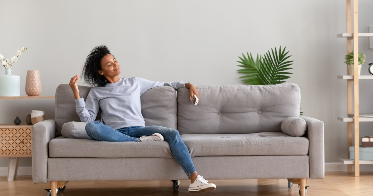 Entspannte Frau, die auf bequemem Sofa im Wohnzimmer im modernen Haus sitzt